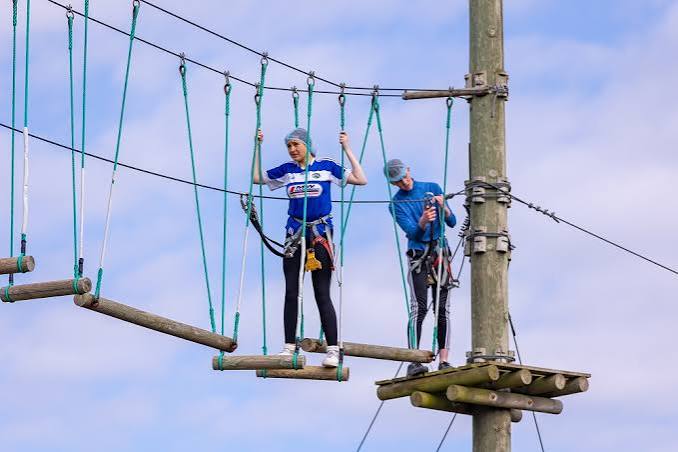 Two people crossing a rope bridge high on the ropes course.