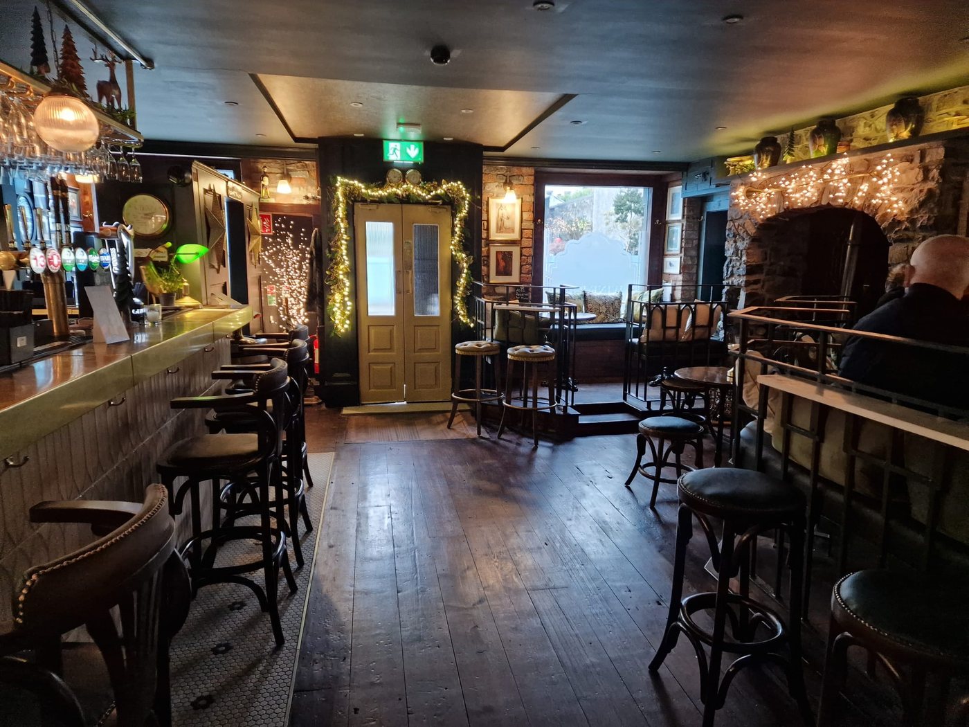 Inside a Carlingford bar: taps and a row of stools along the counter on
                    one side, a stone fireplace hung with lights on the other, and bare
                    floorboards between them.
