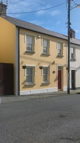 The front of The Retreat on Dundalk Street, Carlingford: a yellow terraced
                townhouse with a red front door and window boxes.