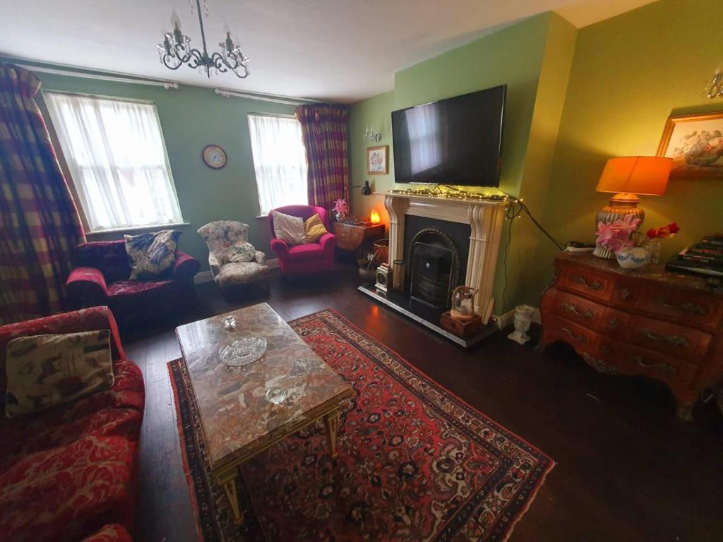The living room from the doorway: two sofas and armchairs round a marble coffee table, an open fire under a white mantel with the television above it, and a chandelier over the rug.