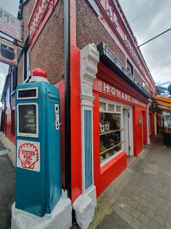 PJ O&rsquo;Hare&rsquo;s in Carlingford: a red and white shopfront lettered
                    H. O&rsquo;Hare Family Grocer, with an old petrol pump painted
                    &ldquo;Oyster Fuel&rdquo; standing on the footpath.